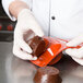 A gloved hand holding a brown round chocolate dessert.