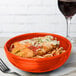 A Fiesta bowl filled with food next to a glass of wine.