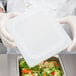 A person holding a white square container with a Vollrath Super Pan V lid filled with broccoli and carrots.