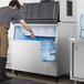 A man in an apron putting a bucket of ice into a Hoshizaki stainless steel ice storage bin.