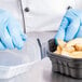 A gloved hand holds a Solo black plastic take-out container of food.