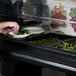 A person preparing food in a black Cambro Versa salad bar.