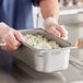 A person in gloves holding a Vigor stainless steel hotel pan of food.