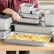 A woman preparing a casserole dish with cheese and bacon in a Vigor stainless steel steam table pan.