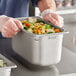 A person holding a Vigor stainless steel pan of food.