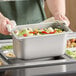 A person holding a Vigor stainless steel pan of broccoli and potatoes.