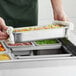 A person holding a Vigor stainless steel steam table pan full of food.