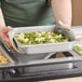 A person holding a Vigor stainless steel steam table pan filled with food.