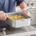 A man in a chef's uniform holding a Vigor stainless steel pan of food.