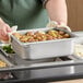 A person holding a Vigor stainless steel pan of food in front of a buffet.