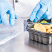 A hand in blue gloves taking food out of a Solo microwaveable plastic container.