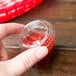 A hand holding a Solo clear plastic souffle lid full of red sauce.