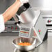 A person using a Hobart commercial food processor to cut carrots in a bowl.