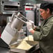 A woman in a chef's uniform using a Hobart full moon pusher food processor to prepare food.