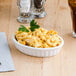 A Tuxton white china oval fluted dish filled with macaroni and cheese on a table.