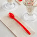 A red Choice plastic soda sundae spoon on a napkin next to a glass of ice cream.