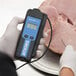 A person using a Cooper-Atkins AquaTuff thermocouple thermometer to measure the temperature of a ham.