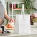 A woman holding a white Choice market stand bag on a table.