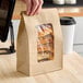 A brown kraft paper bag with a clear window displaying pastries inside.