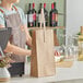 A person in an apron standing behind a counter with a brown paper bag with a handle holding two bottles of liquid.