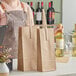 A woman standing behind a counter holding a brown paper wine bag with two bottles in it.