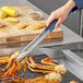 A person using Vollrath stainless steel tongs to pick up a crab claw.