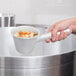 A person holding a Vollrath aluminum dipper over a pot of soup.