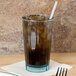 A close-up of a Cambro azure blue polycarbonate tumbler filled with brown liquid and ice with a straw.