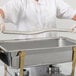 A person in white gloves using a Vollrath Adapter Bar to hold a metal container in a chafing dish.