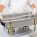 A person in gloves holding a Vollrath long stainless steel steam table pan adapter bar.