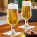 Two Libbey stemmed pilsner glasses filled with beer on a table.