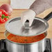 A person wearing gloves is holding a Vollrath Tribute pan cover over a pot of soup.