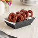 A black rectangular plastic fast food basket filled with pretzels on a table.