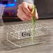 A hand holding a test tube with green liquid in a clear plastic test tube shot rack.
