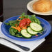 A Carlisle ocean blue melamine plate with a salad and a fork on a table with more salad plates.