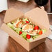 A box of salad with a knife and fork on the table.