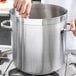 A person holding a wooden spoon in a large silver stock pot.