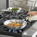 A person using a Vollrath Wear-Ever fry pan to cook food on a stove.