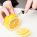 A person's hand using a Dexter-Russell V-Lo scalloped paring knife to slice a lemon.