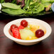 A Carlisle tan melamine fruit bowl on a table with fruit.