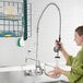 A woman using an Equip by T&amp;S wall mounted pre-rinse faucet to wash dishes over a sink.