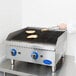 A person in a white coat cooking food on a Globe gas charbroiler.