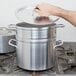 A hand holding a silver lid over a large silver pot.