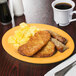 A tropical yellow oval melamine platter with food including scrambled eggs and a cup of coffee on a table.