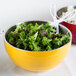 A Vollrath Nugget Yellow metal serving bowl filled with salad, with a fork and spoon.