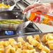 A person spraying Vegalene Canola Release Spray on a pan of potatoes.