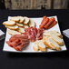 An American Metalcraft square concave melamine platter with sliced meats and bread on it.