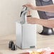 A person using a chrome pump to pour liquid into a container on a counter.