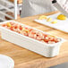 A person cutting a lemon on a cutting board with a tray of shrimp using a Cambro white polycarbonate food pan.