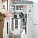 A man pouring water from a glass into a Hobart floor mixer.